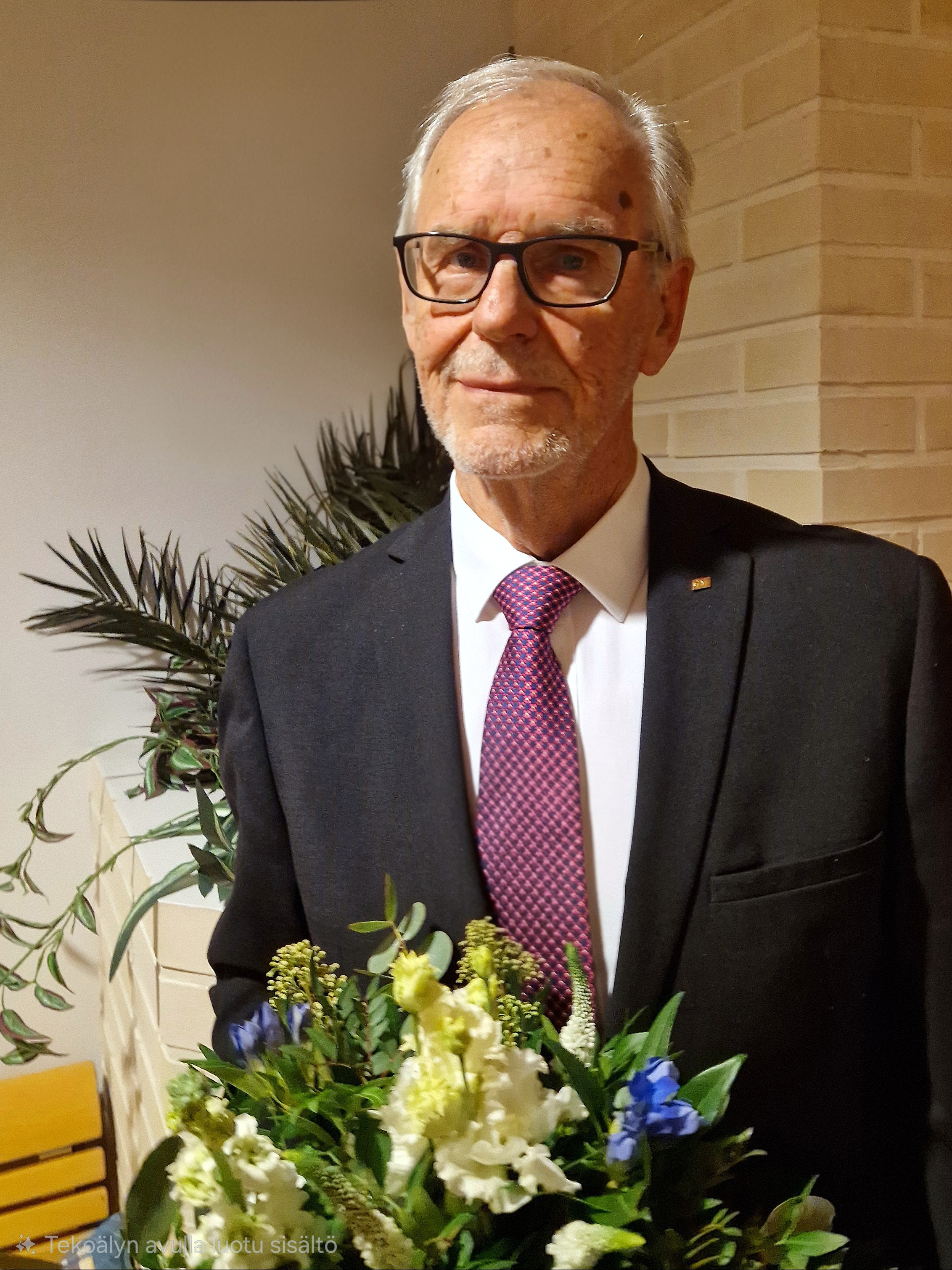 Asessori Pekka Ritvanen sinivalkoinen kukkakimppu kädessä.