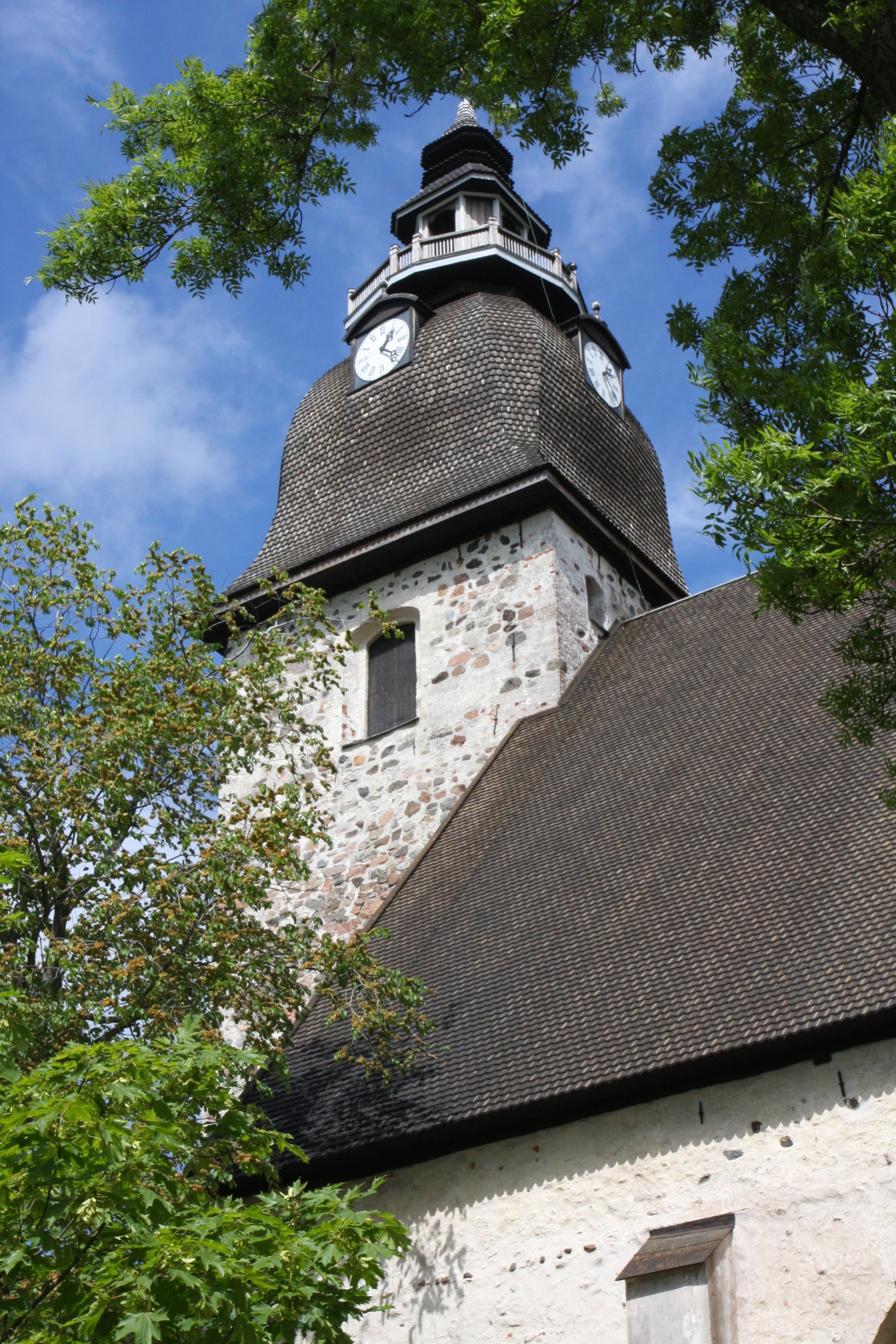 Naantalin kirkon torni kuvattuna Kirkkopuiston puolelta. Ympärillä vihreälehtisiä puunoksia.